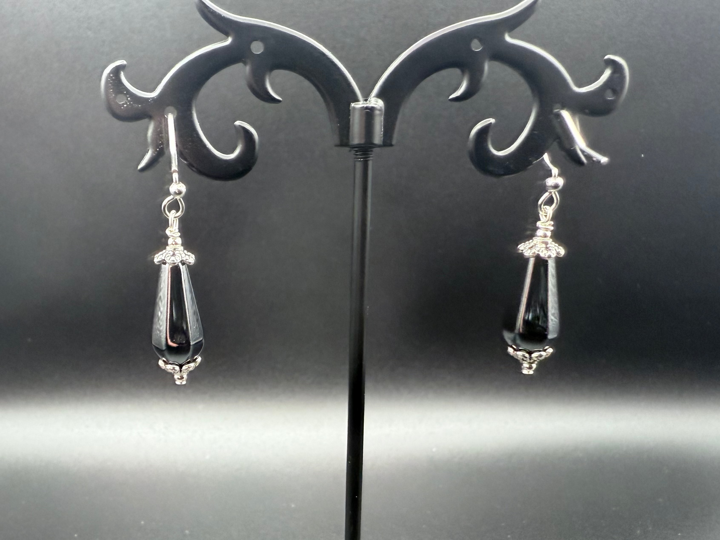 Shiny, dark gray and silver earrings on a decorative stand against a dark background