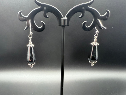 Shiny, dark gray and silver earrings on a decorative stand against a dark background
